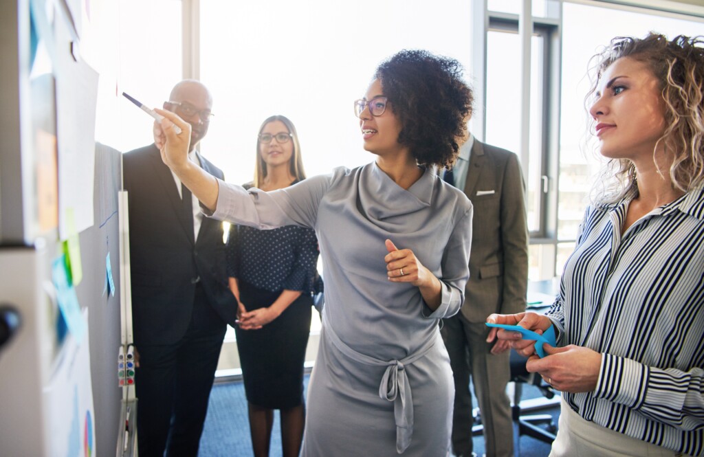 A diverse group of professionals in front of a whiteboard engaged in a strategic conversations bootcamp.