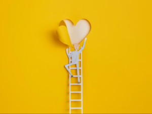 Paper cutout of a person on top of a ladder peeling back a heart which is meant to symbolize unlocking your passion - referred to in this article as ikigai