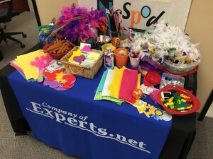 Creativity kit table during an appreciative inquiry training displays creative items intended to invite play and spark innovation and can include items such as: feather boas, tissue paper, colorful pipe cleaners, masks, stickers, and post-its,